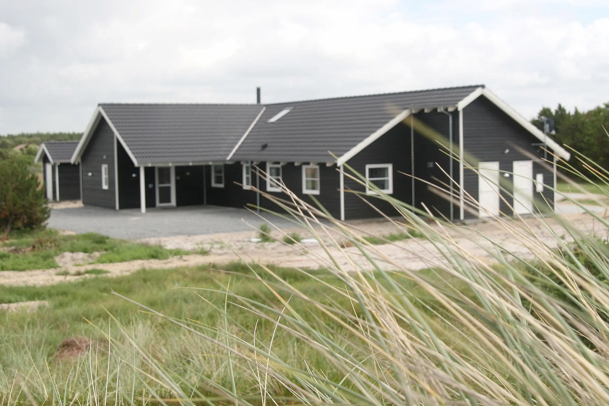 A holiday home situated near the North Sea (Vesterhavet) with grass and marram grass in the foreground, highlighting the coastal landscape.