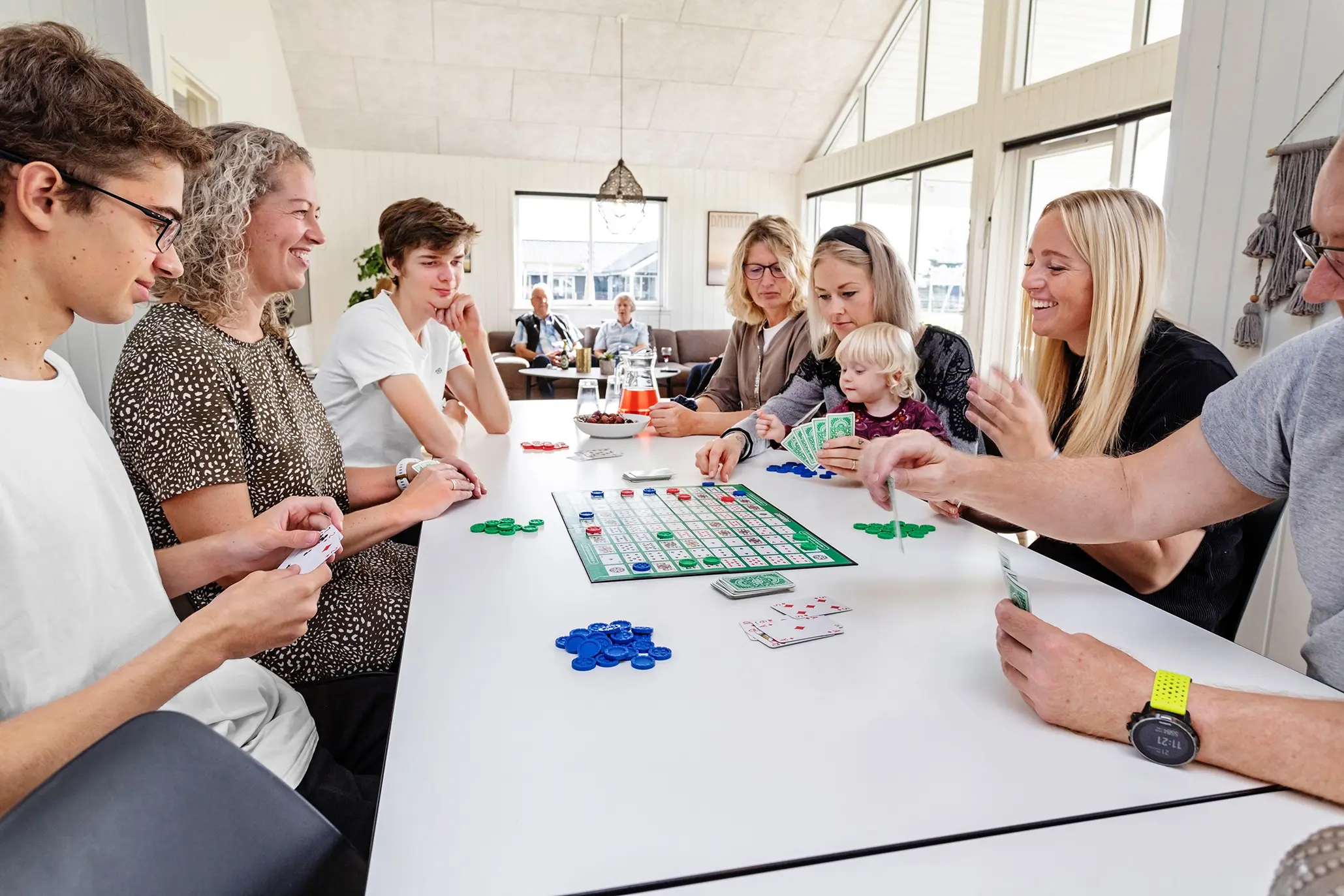 Glade børn og voksne sidder ved bord og spiller brætspil