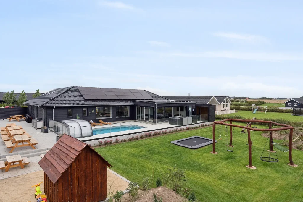 stort luksus-sommerhus med udendørs pool og græsplæne med legeplads